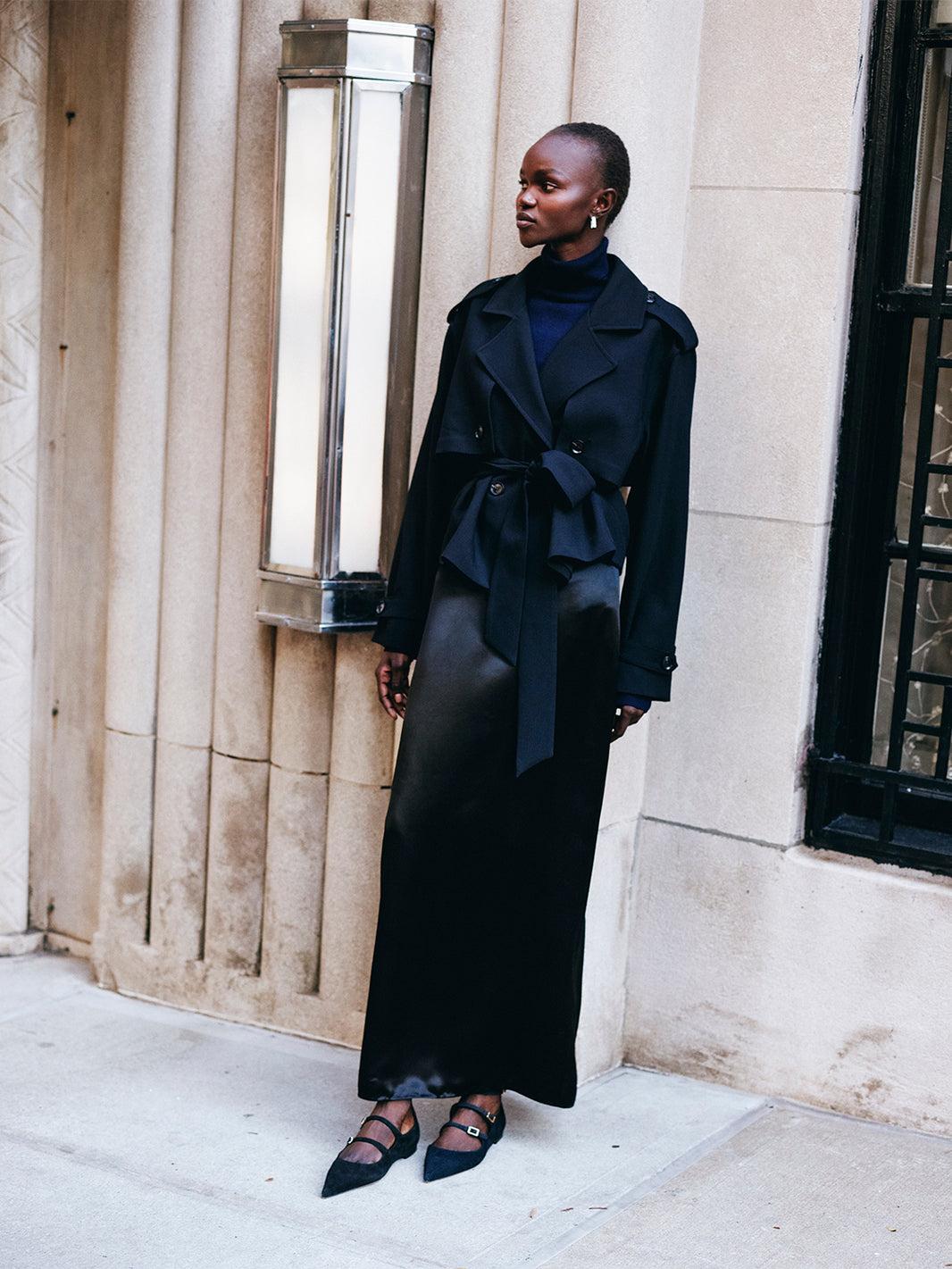 Angle view of a black suede mary jane flat with adjustable straps and a pointed toe, shown on a model. 