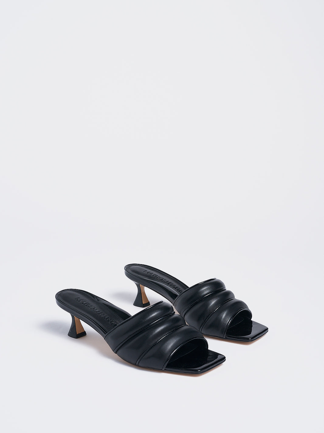 Angle view of a pair of black leather slide kitten heels with a patent leather trimmed puffy strap detail.