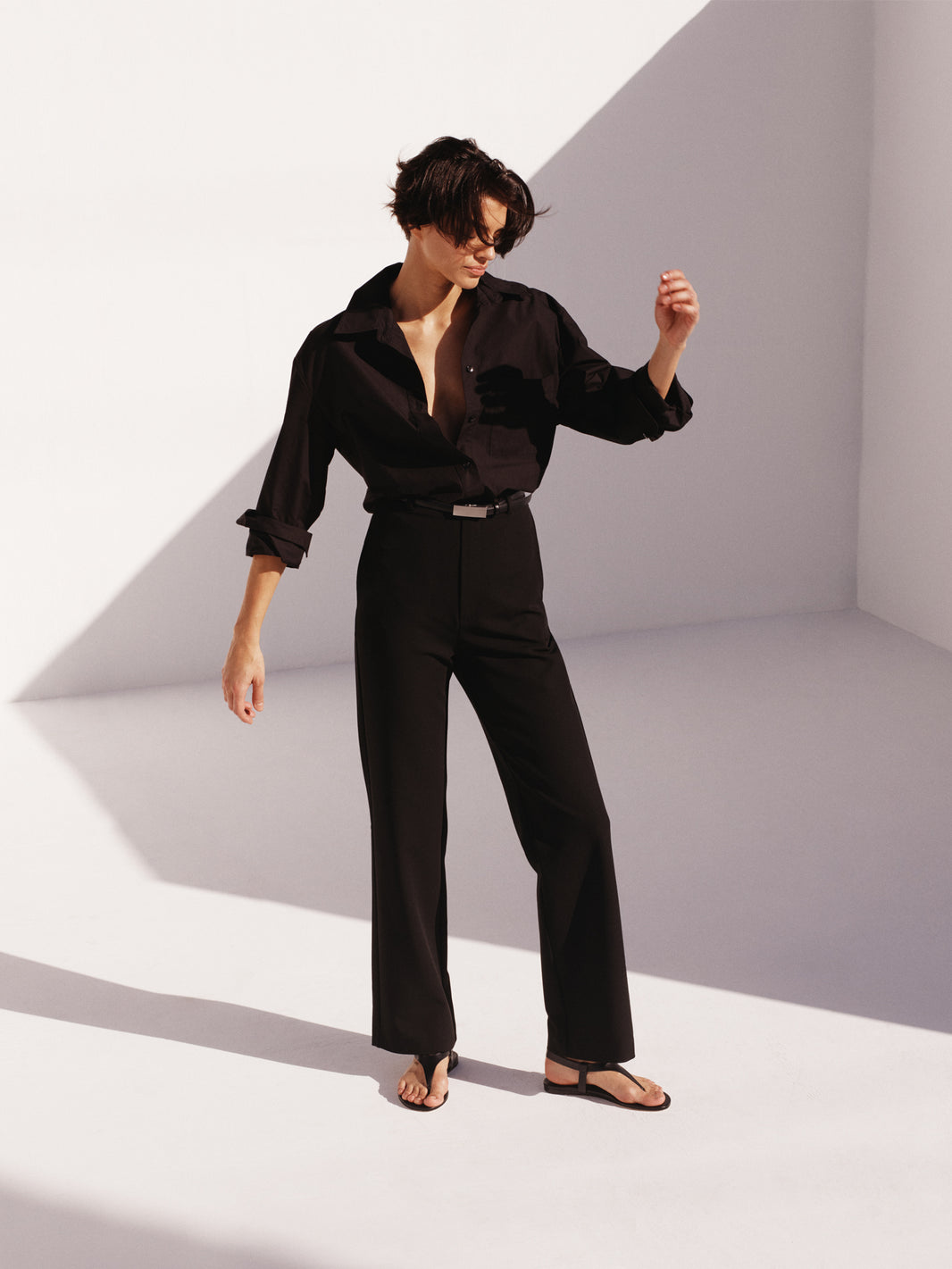 Black leather thong sandal with a clean design and adjustable ankle strap, shown on a model. 