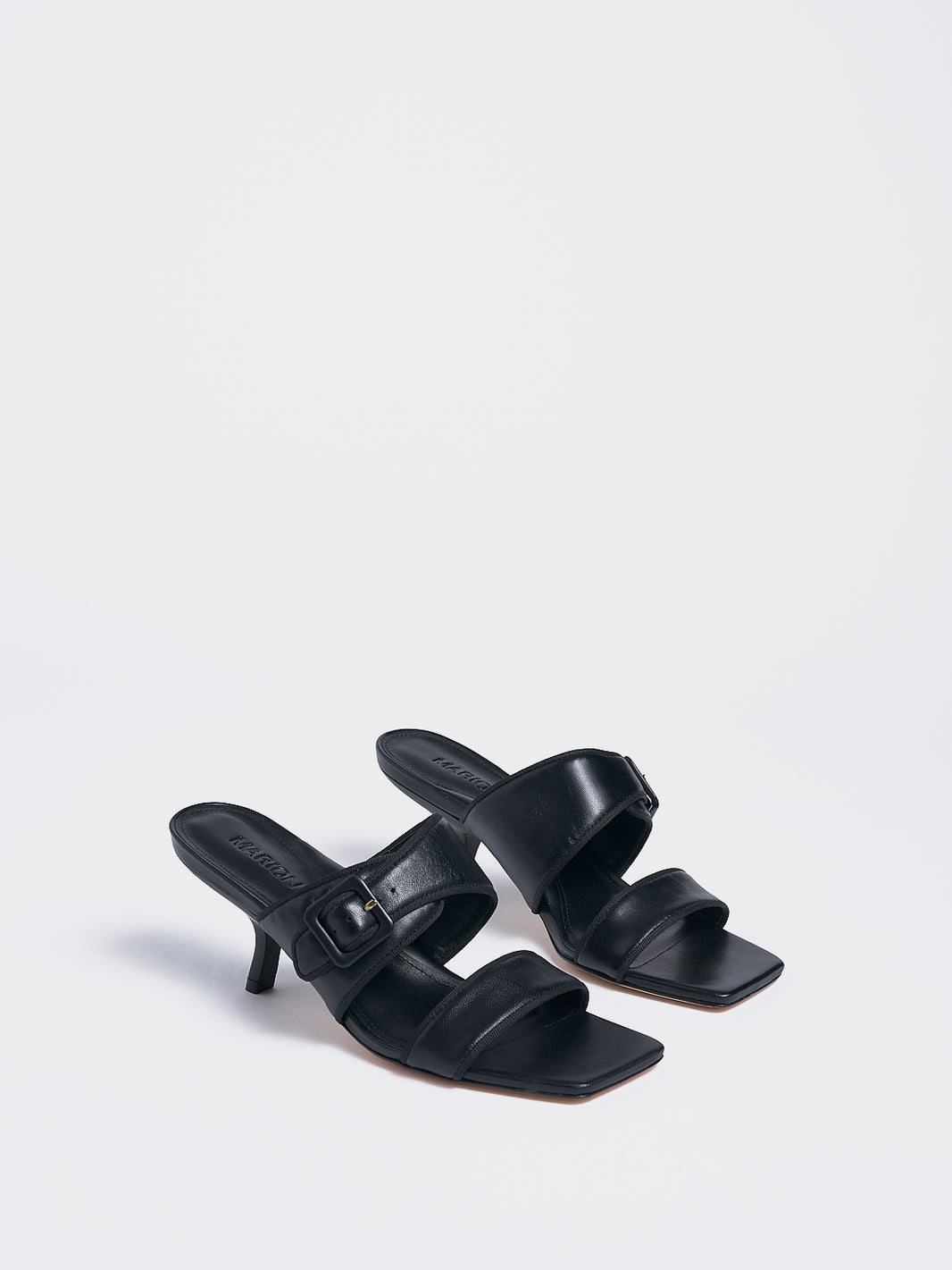 Angle view of a pair of black leather slide kitten heel sandals with a buckle detail.