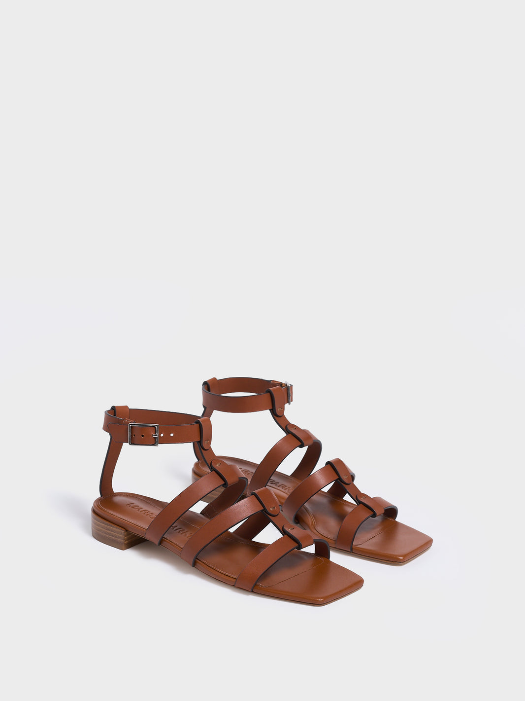 Angle view of a pair of chestnut leather gladiator sandals with an adjustable ankle strap.