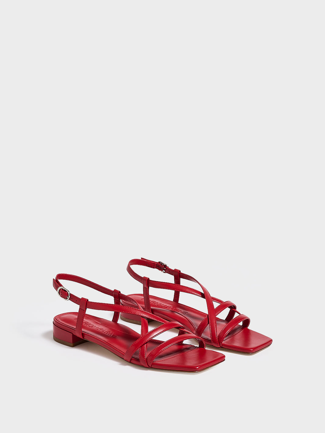 Angle view of a pair of lipstick red leather flat strappy sandals.