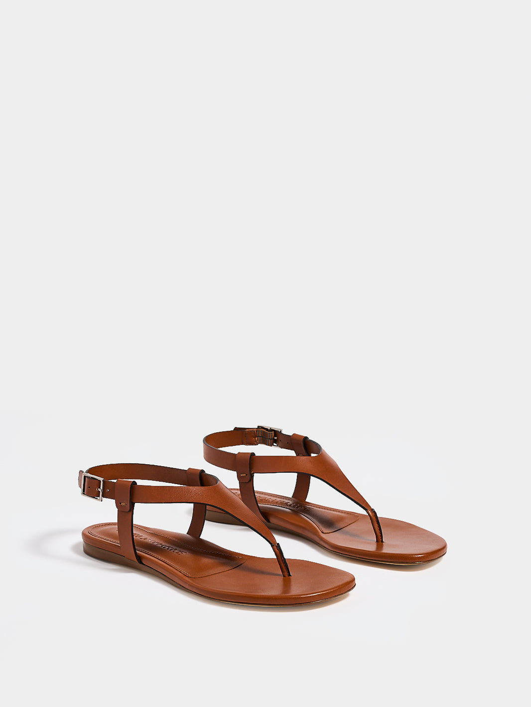 Angle view of a pair of chestnut leather thong sandals with a clean design and adjustable ankle strap. 