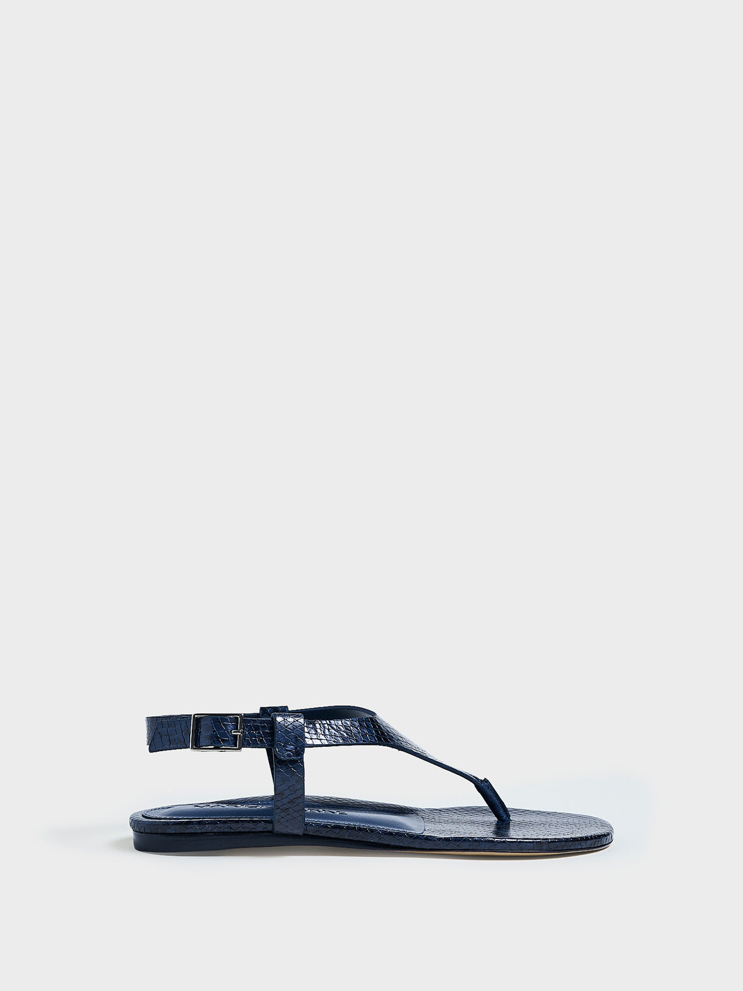 Profile view of a navy python leather thong sandal with a clean design and adjustable ankle strap. 