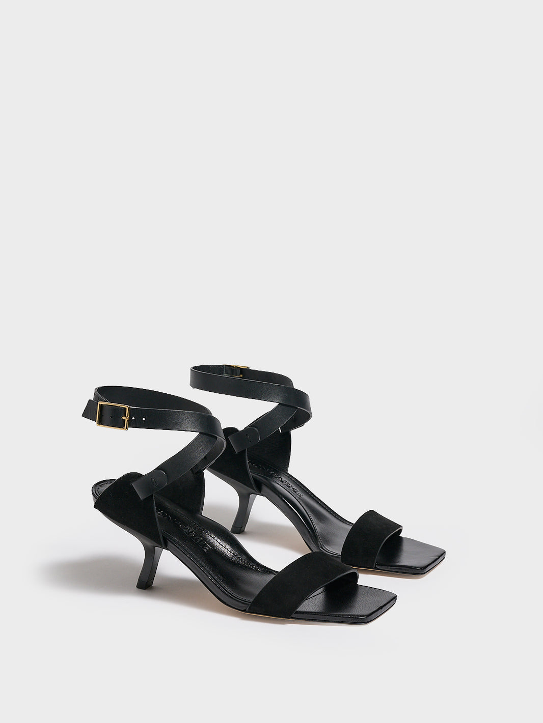 Angle view of a pair of black leather and suede high heel sandals with a sculptural design and adjustable ankle strap. 